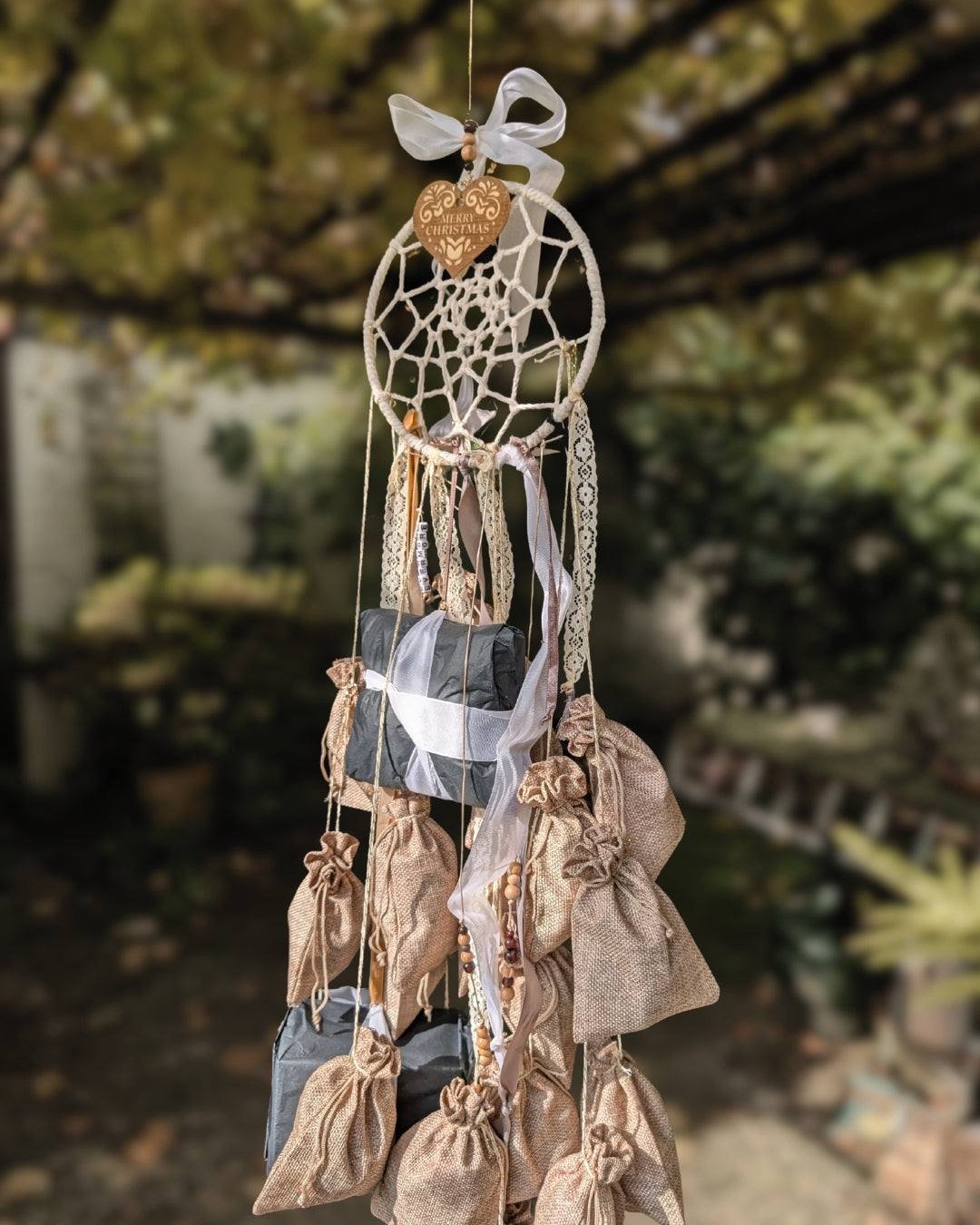 Medium Longshot des handgemachten Hoggynook Adventskalenders: kleine nummerierte Stoffbeutel am Dreamcatcher, verziert mit Schleifen, Spitze und Satinbändern. Detailshot zeigt hochwertige Handarbeit und rustikale Winter-Ästhetik. Perfekte Kombination aus Boho, Dark Academia und Weihnachtsdekoration für Buchliebhaberinnen.