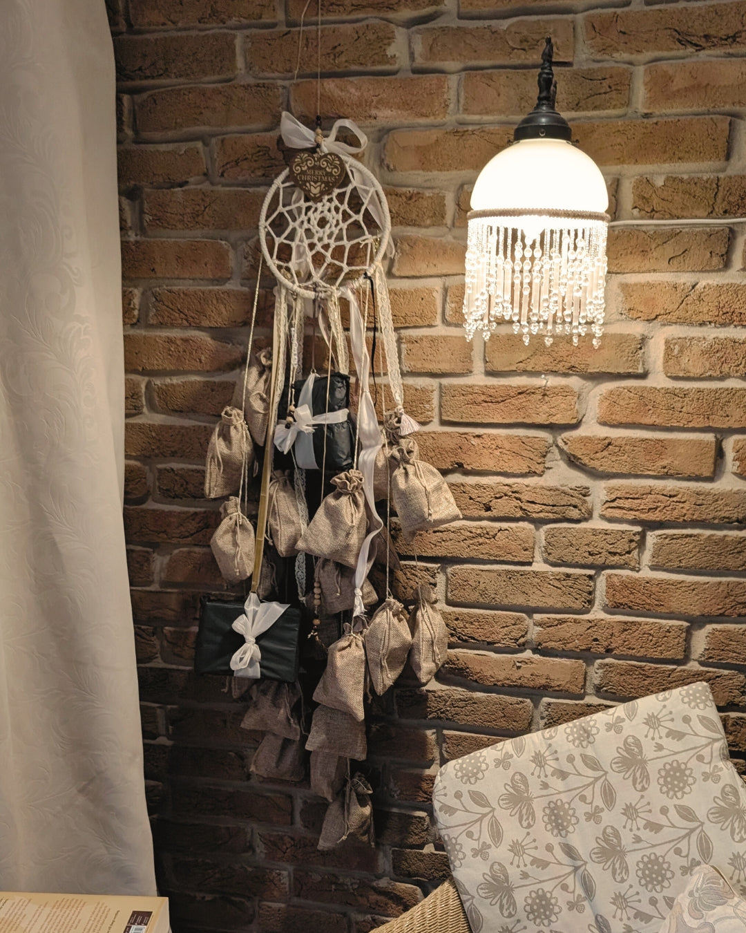 Handgemachter Adventskalender Dreamcatcher von Hoggynook, 1,20m lang, dekoriert mit 24 nummerierten Stoffbeuteln, Spitze und Satinbändern. Präsentiert in gemütlicher Weihnachts-Szene mit Lichterkette, Kerzen, Tannenzapfen und Hygge-Stimmung. Einzigartige Adventskalender-Idee, Boho- und Dark-Academia-Stil, perfekte Geschenkidee für Buchliebhaberinnen und Booktok-Fans.