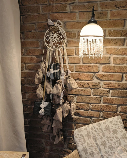 Handgemachter Adventskalender Dreamcatcher von Hoggynook, 1,20m lang, dekoriert mit 24 nummerierten Stoffbeuteln, Spitze und Satinbändern. Präsentiert in gemütlicher Weihnachts-Szene mit Lichterkette, Kerzen, Tannenzapfen und Hygge-Stimmung. Einzigartige Adventskalender-Idee, Boho- und Dark-Academia-Stil, perfekte Geschenkidee für Buchliebhaberinnen und Booktok-Fans.